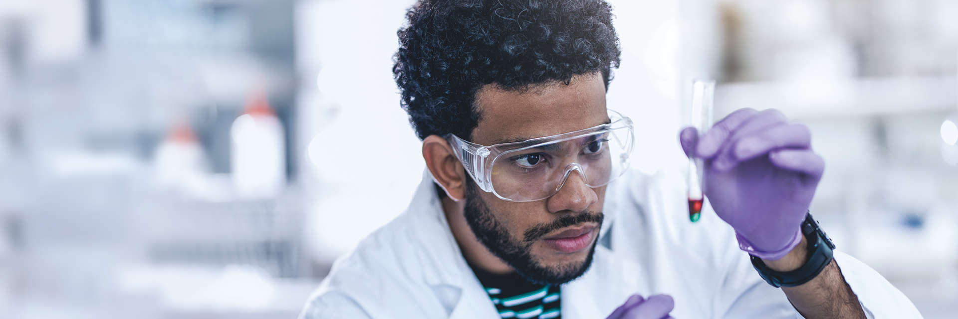 Enzymes, NGS, Black male scientist looking at test-tube filled with substance in a laboratory setting